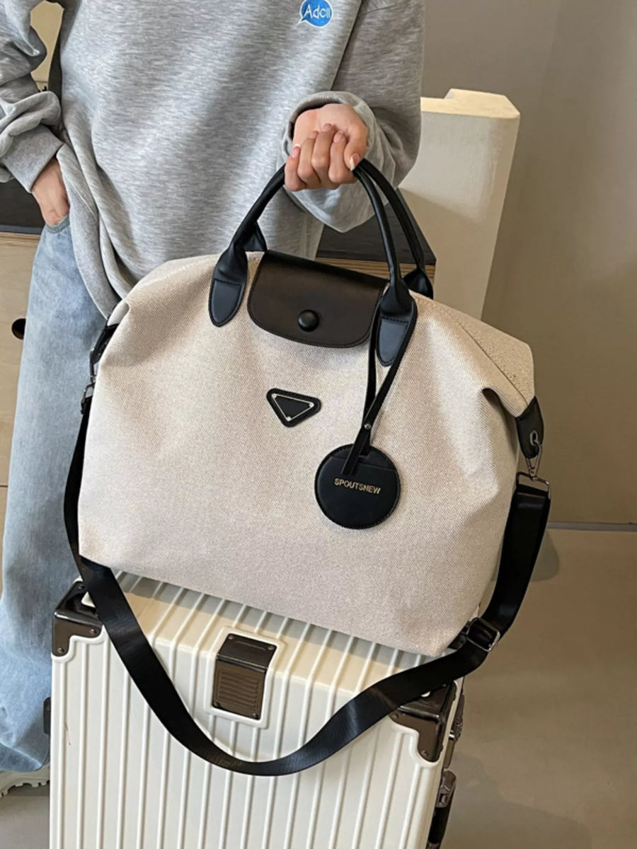 Person holding a beige handbag with black straps on a white suitcase.