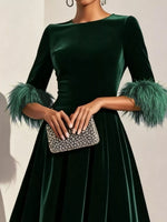 Green dress with feathered sleeves held by a hand with a clutch against a neutral background