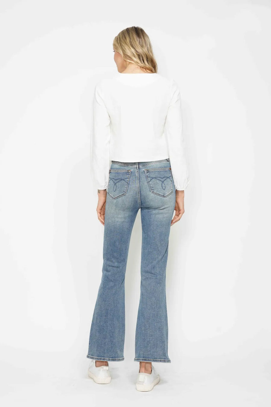 Person wearing light blue flared jeans and a white top on a white background