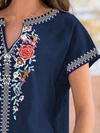Navy blue dress with colorful floral embroidery on a blurred natural background