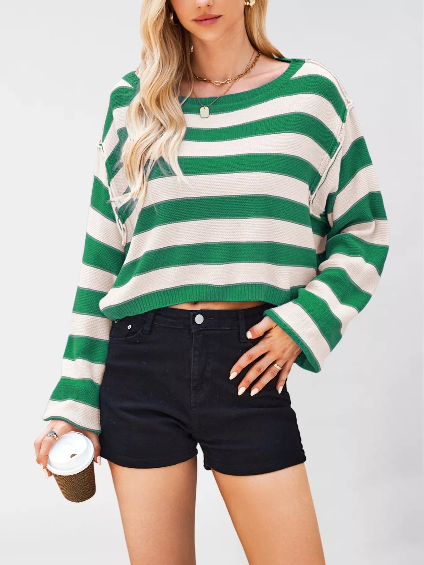 Person wearing a green and white striped sweater with black shorts on a plain background
