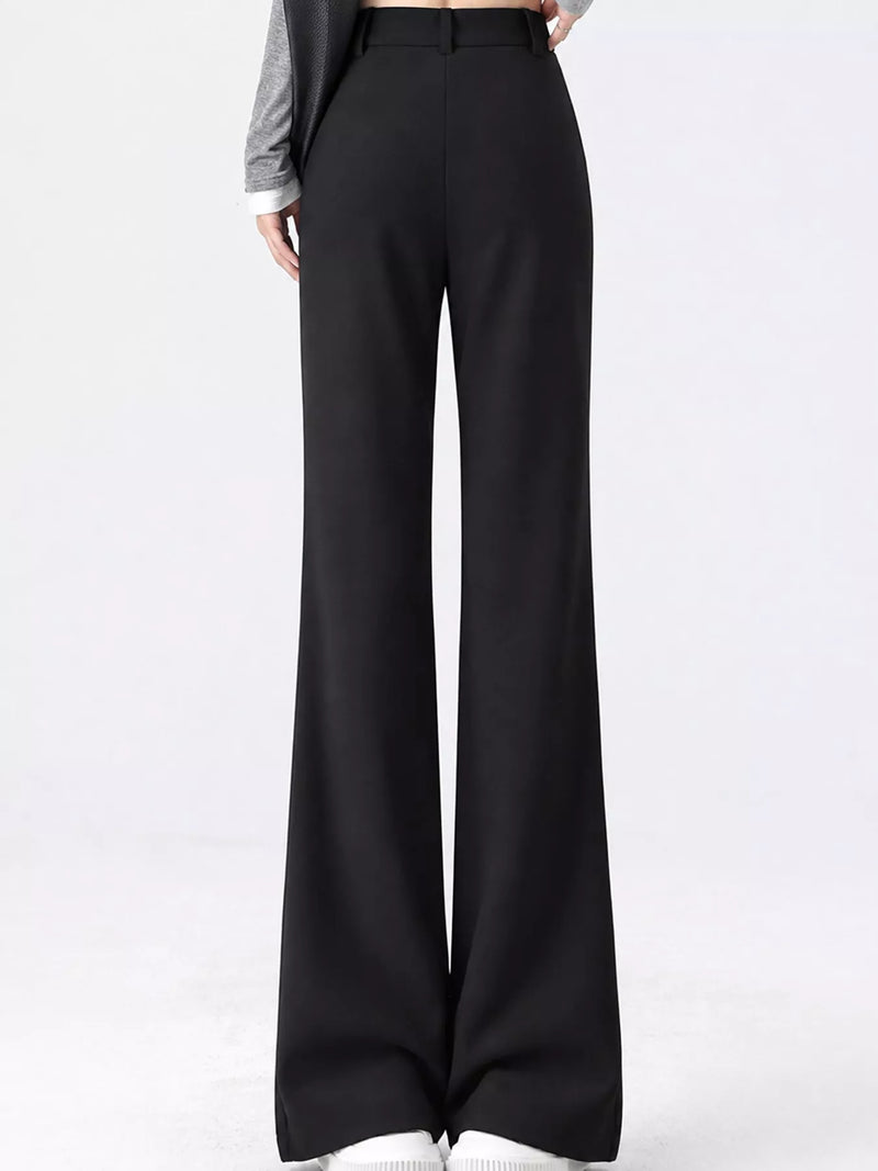 Black wide-leg trousers shown on a model from the waist down, paired with a gray long-sleeve top and white sneakers against a plain white studio background.