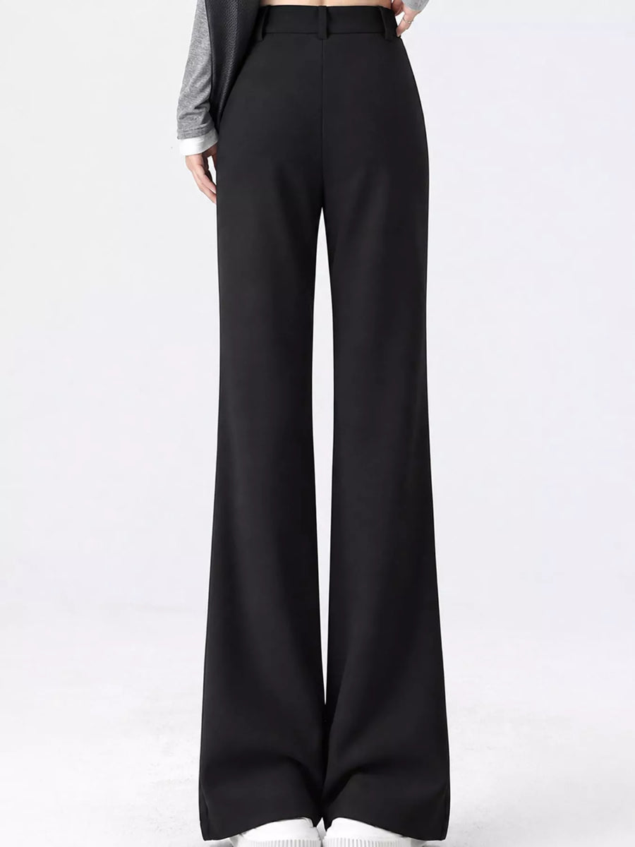 Black wide-leg trousers shown on a model from the waist down, paired with a gray long-sleeve top and white sneakers against a plain white studio background.