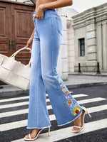 Person wearing light blue jeans with floral embroidery on a city street.