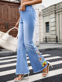 Person wearing light blue jeans with floral embroidery on a city street.