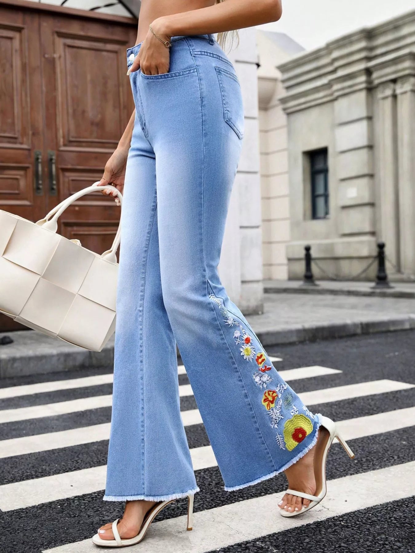 Person wearing light blue jeans with floral embroidery on a city street.