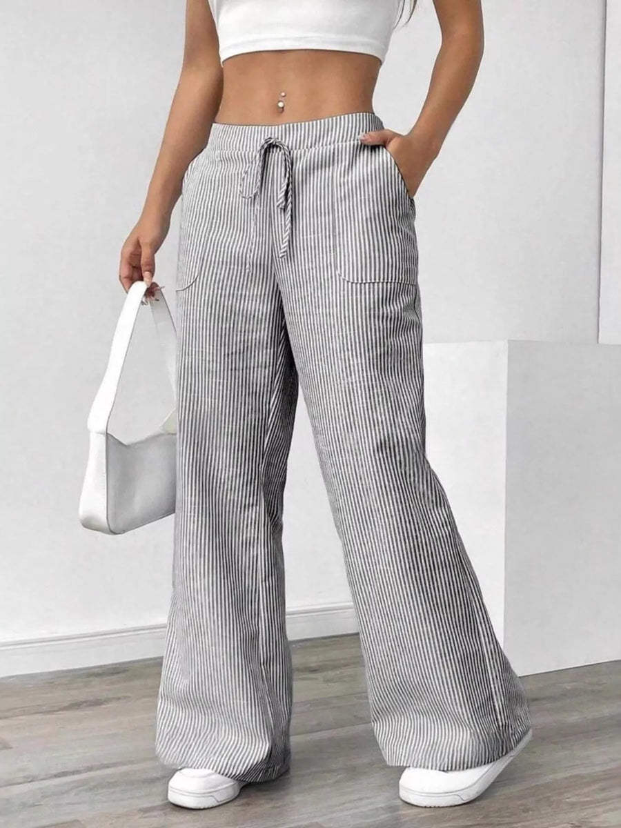 Person wearing gray striped wide-leg pants with a white top and white shoes on a plain background