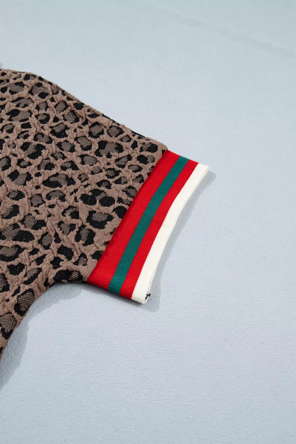 Leopard print glove with red, green, and white striped cuff on a light blue background
