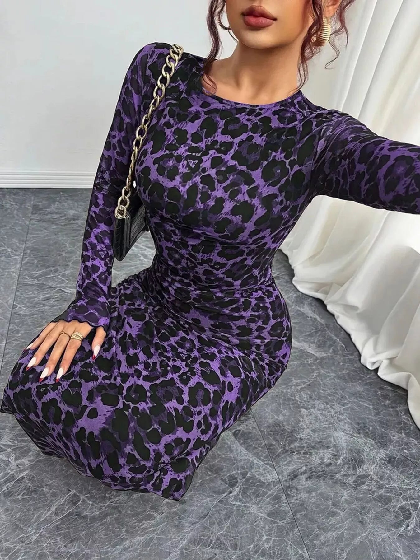Person wearing a purple leopard print dress with a gold handbag indoors.