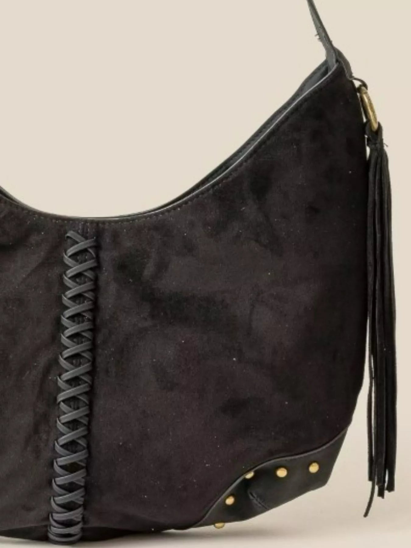 Black handbag with braided strap and tassel on a beige background
