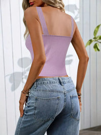 Person wearing a light purple tank top and blue jeans against a white wall.