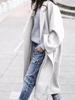 Person wearing a long gray coat over a light blue sweater and jeans on a blurred background