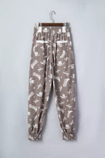 Brown pants with white pattern on a hanger against a light gray background