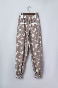 Brown pants with white pattern on a hanger against a light gray background