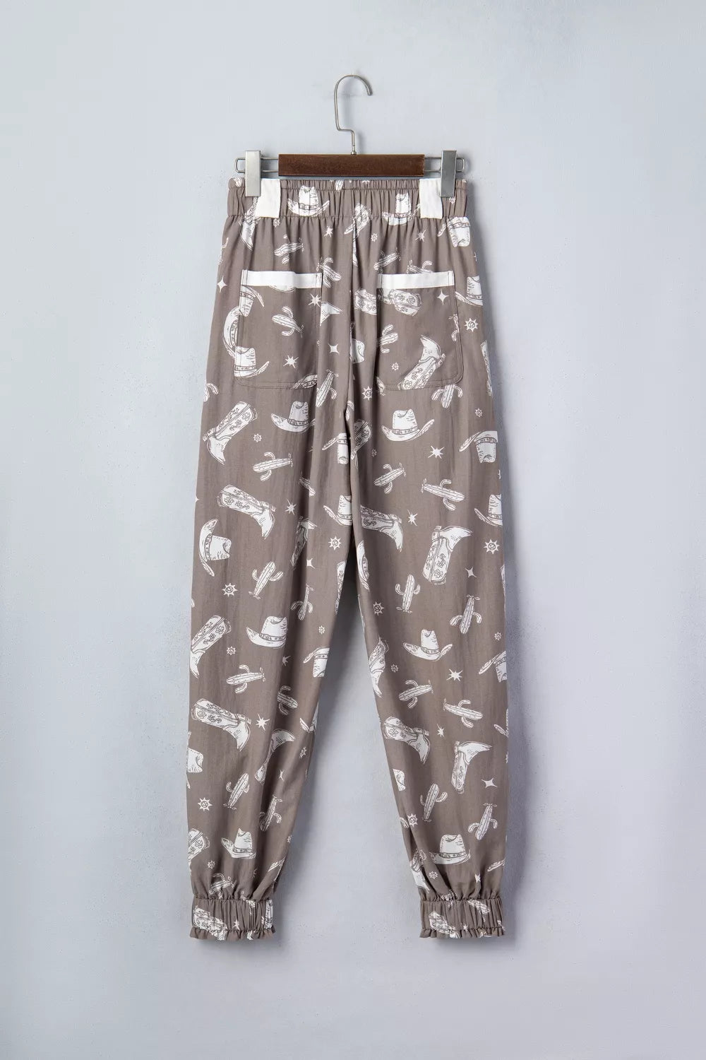Brown pants with white pattern on a hanger against a light gray background