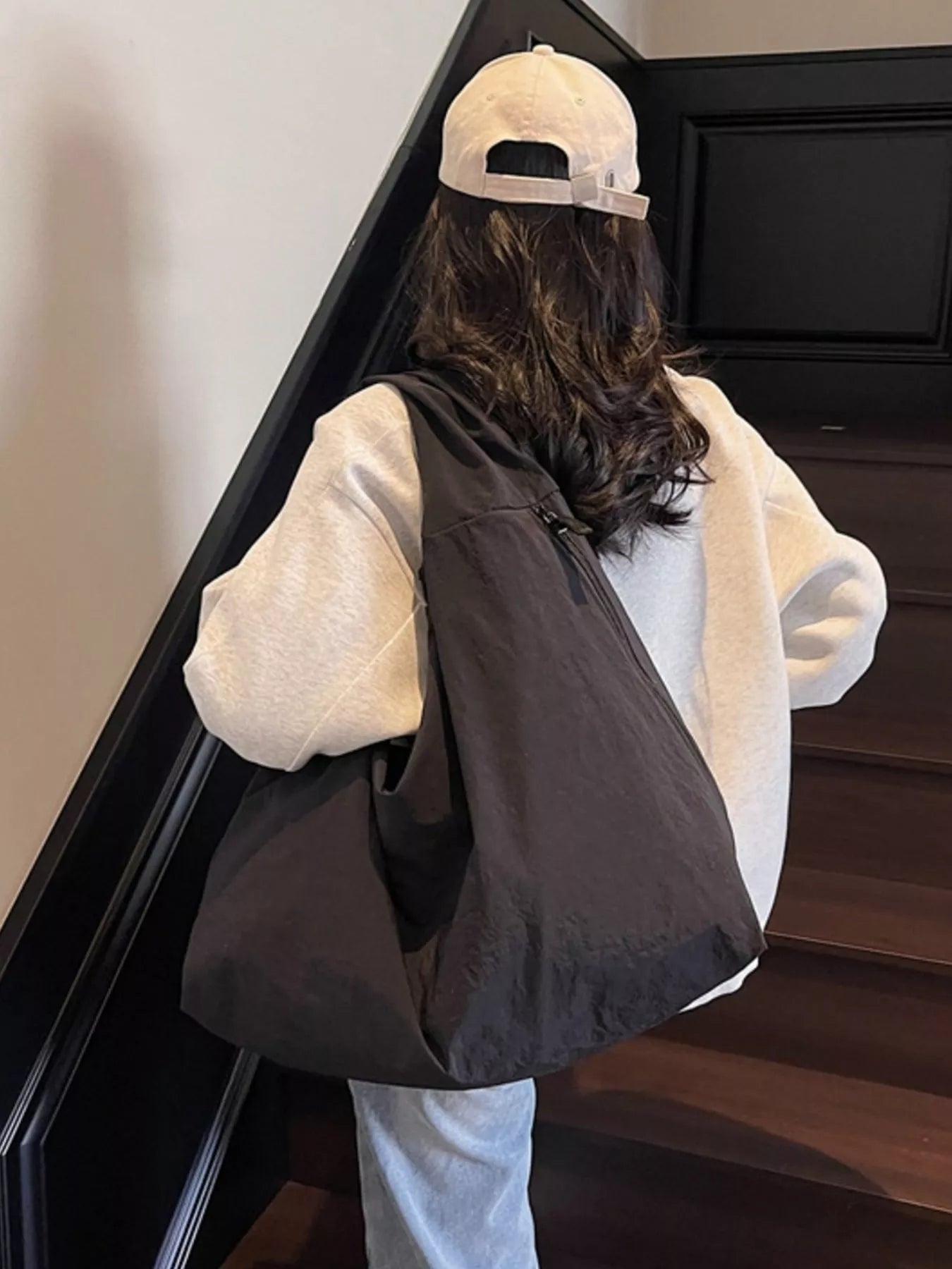 Person wearing a white hoodie, black vest, and beige cap walking up a staircase.