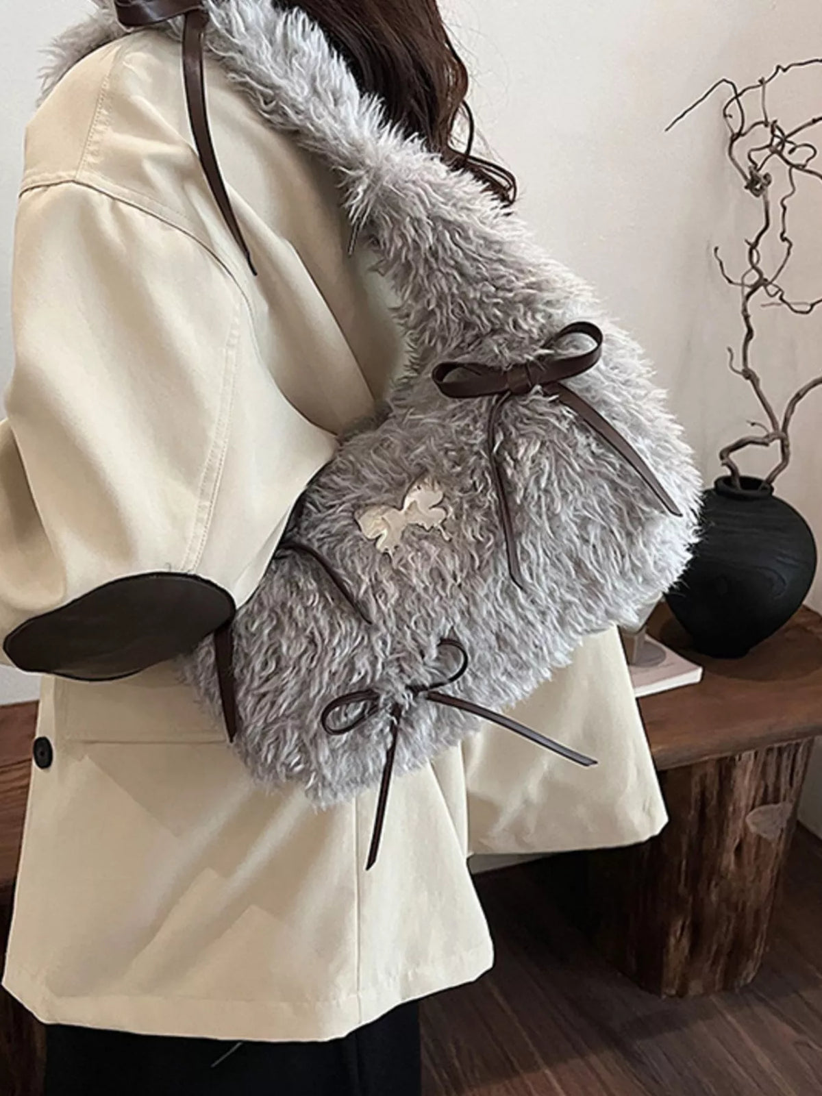 Person wearing a beige coat with gray fur-lined mittens indoors.