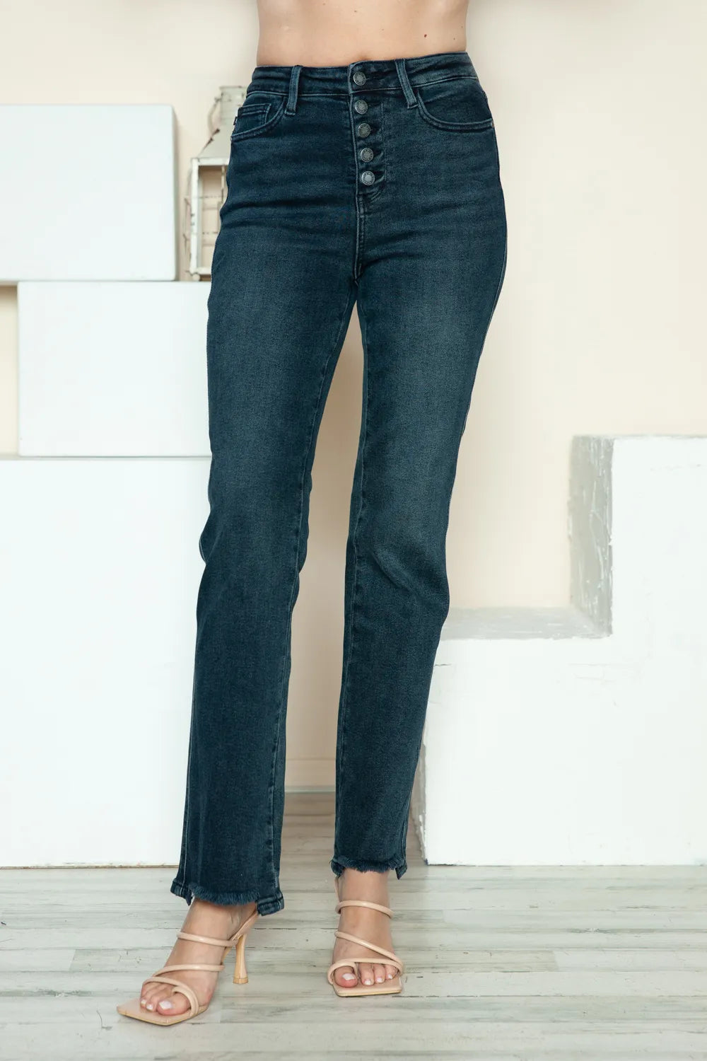 Dark blue jeans worn by a person standing indoors with a neutral background
