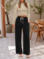 Woman wearing a beige long-sleeve top and black wide-leg pants in an outdoor setting.