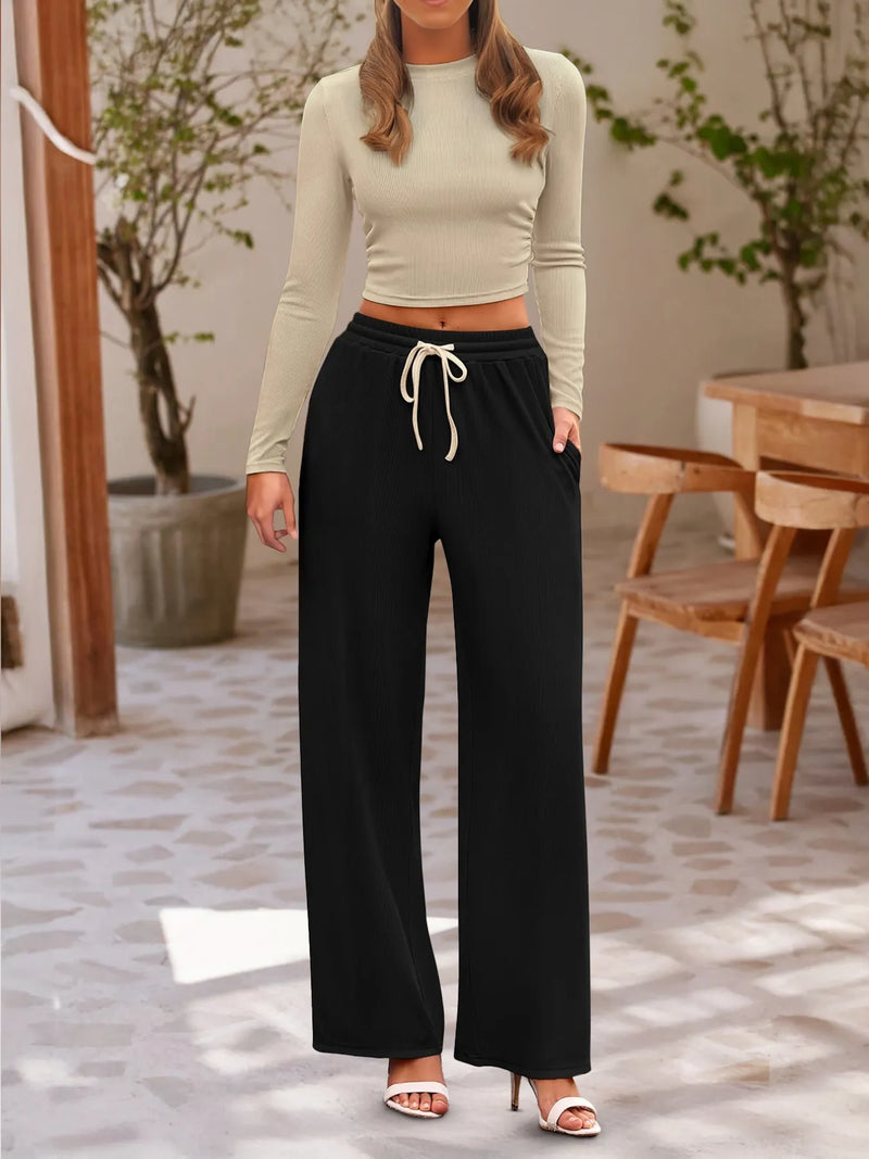 Woman wearing a beige long-sleeve top and black wide-leg pants in an outdoor setting.
