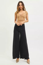 Woman wearing a beige top and black wide-leg pants on a white background