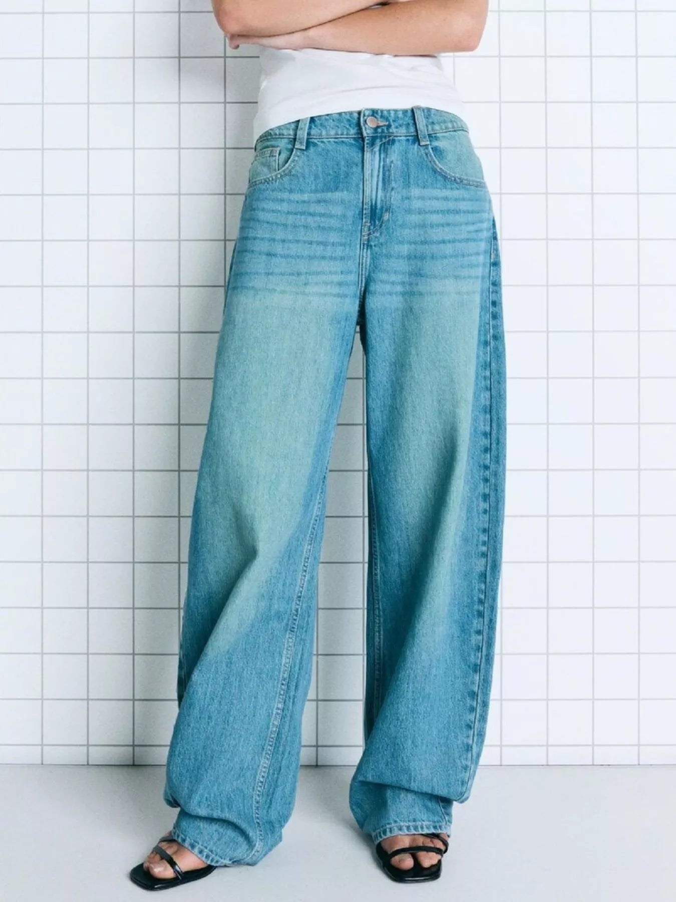 Person wearing blue jeans against a white tiled wall