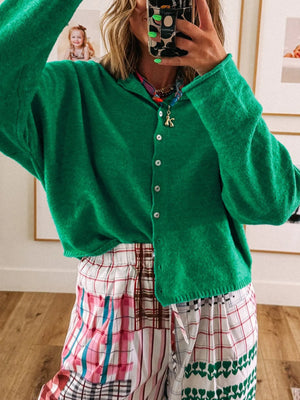 Person wearing a green cardigan over a colorful plaid dress, standing indoors.