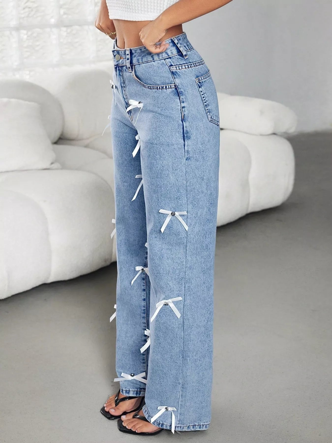 Light blue jeans with white bows worn by a person in a minimalistic room.