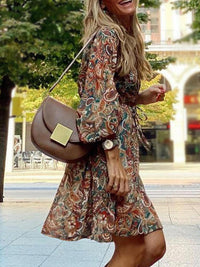 Woman in a patterned dress holding a brown handbag outdoors.