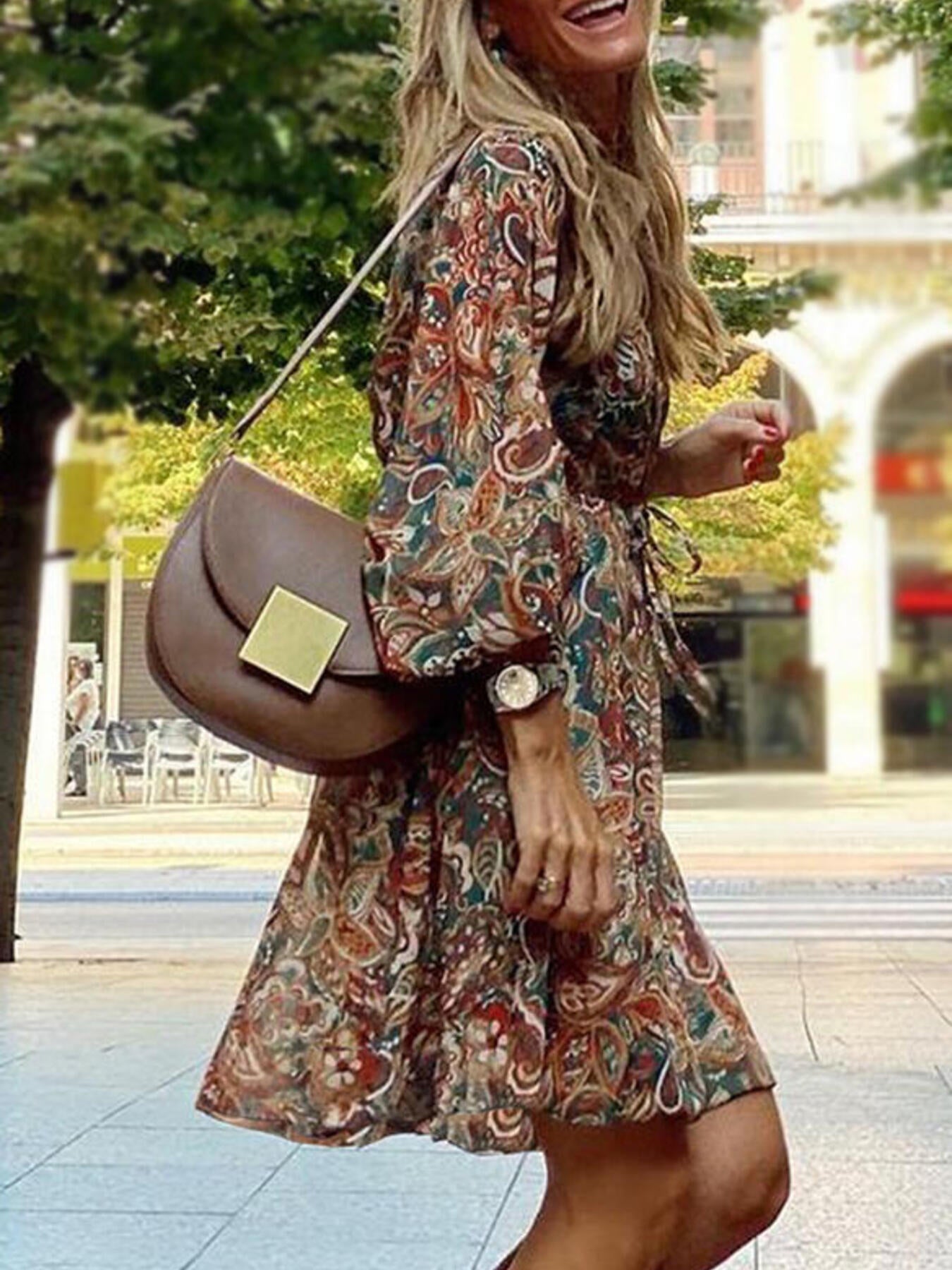 Woman in a patterned dress holding a brown handbag outdoors.