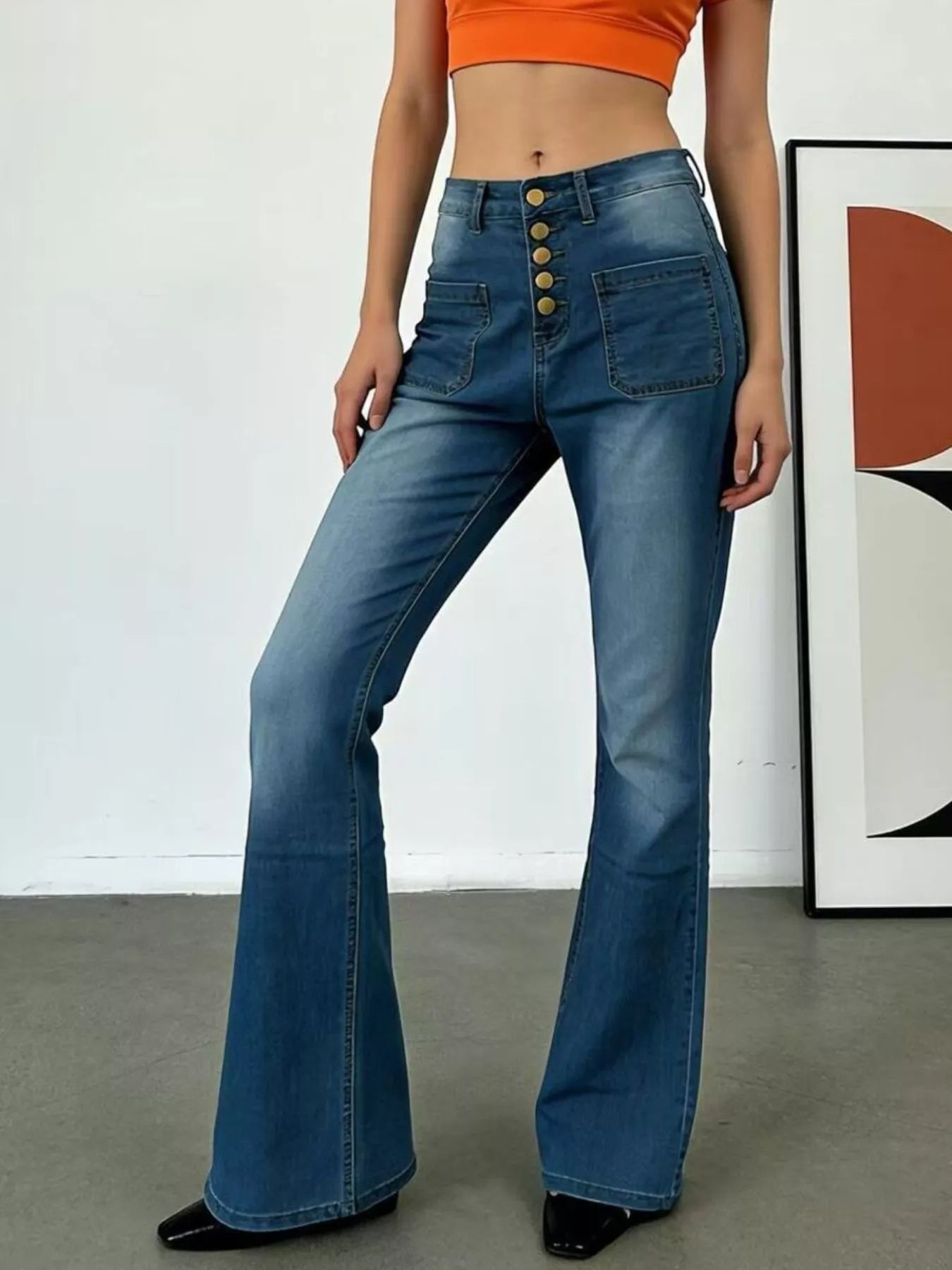 Person wearing blue flared jeans with a white wall and abstract art in the background