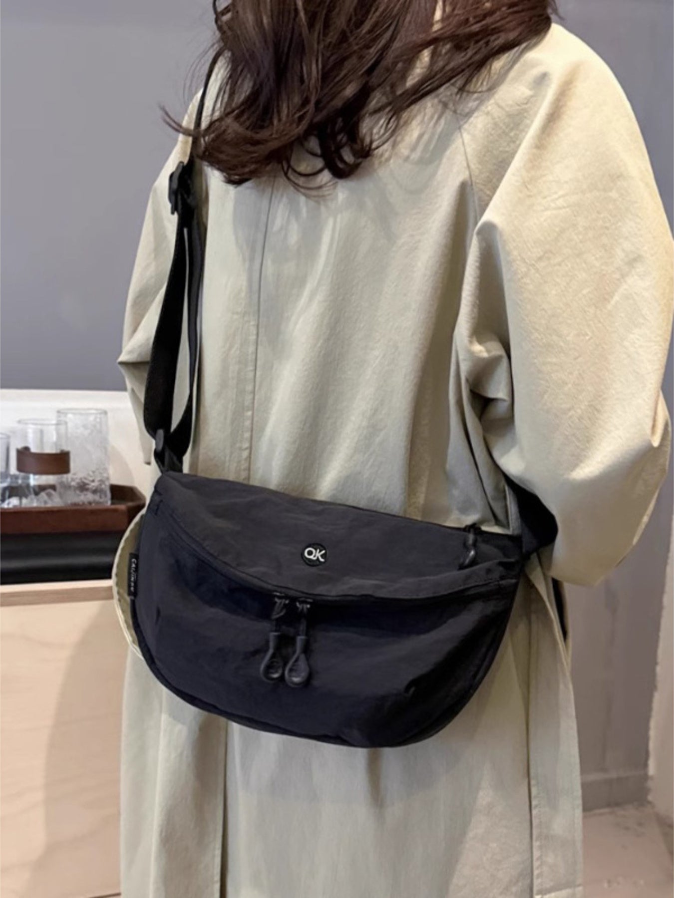 Person wearing a black crossbody bag with a visible brand logo in an indoor setting.