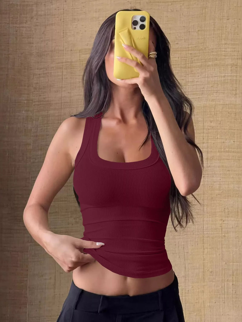 Woman wearing a red tank top taking a mirror selfie against a textured brown wall.