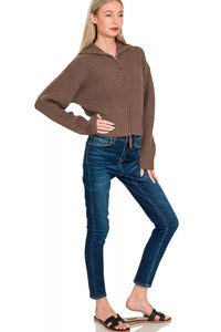 Woman wearing a brown sweater and blue jeans on a white background