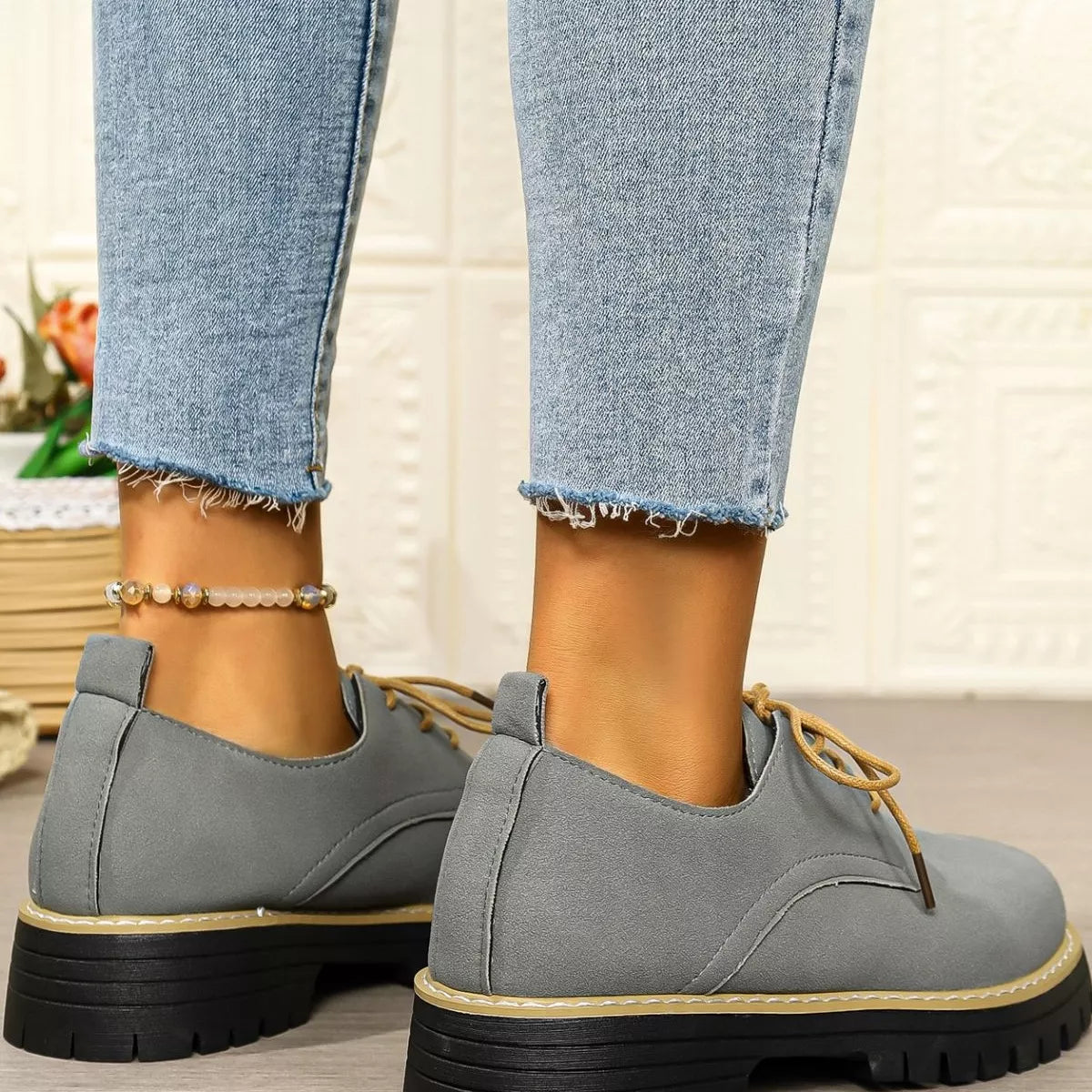 Gray shoes with black soles worn with light blue jeans on a neutral background