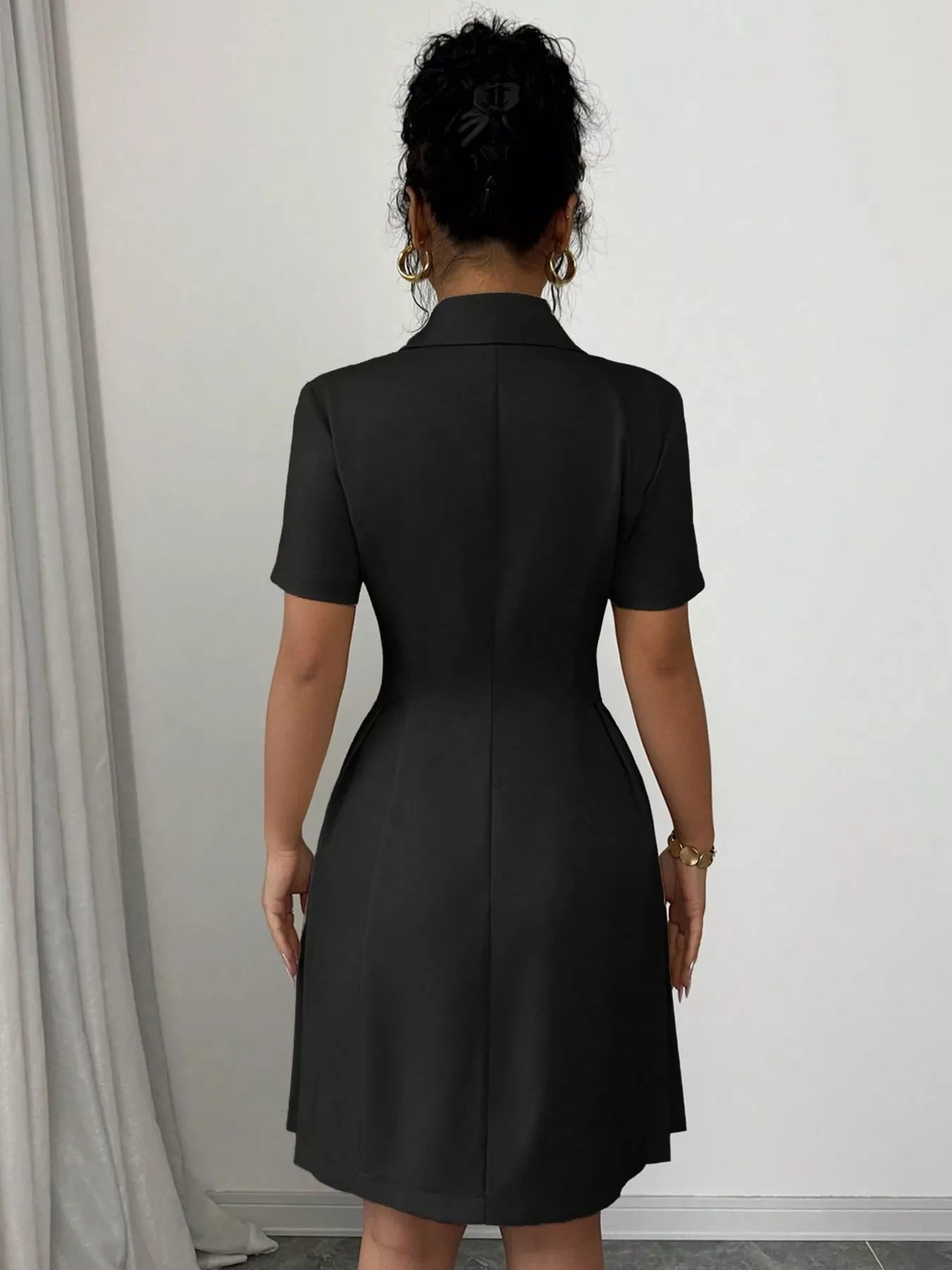Person wearing a black dress against a white wall