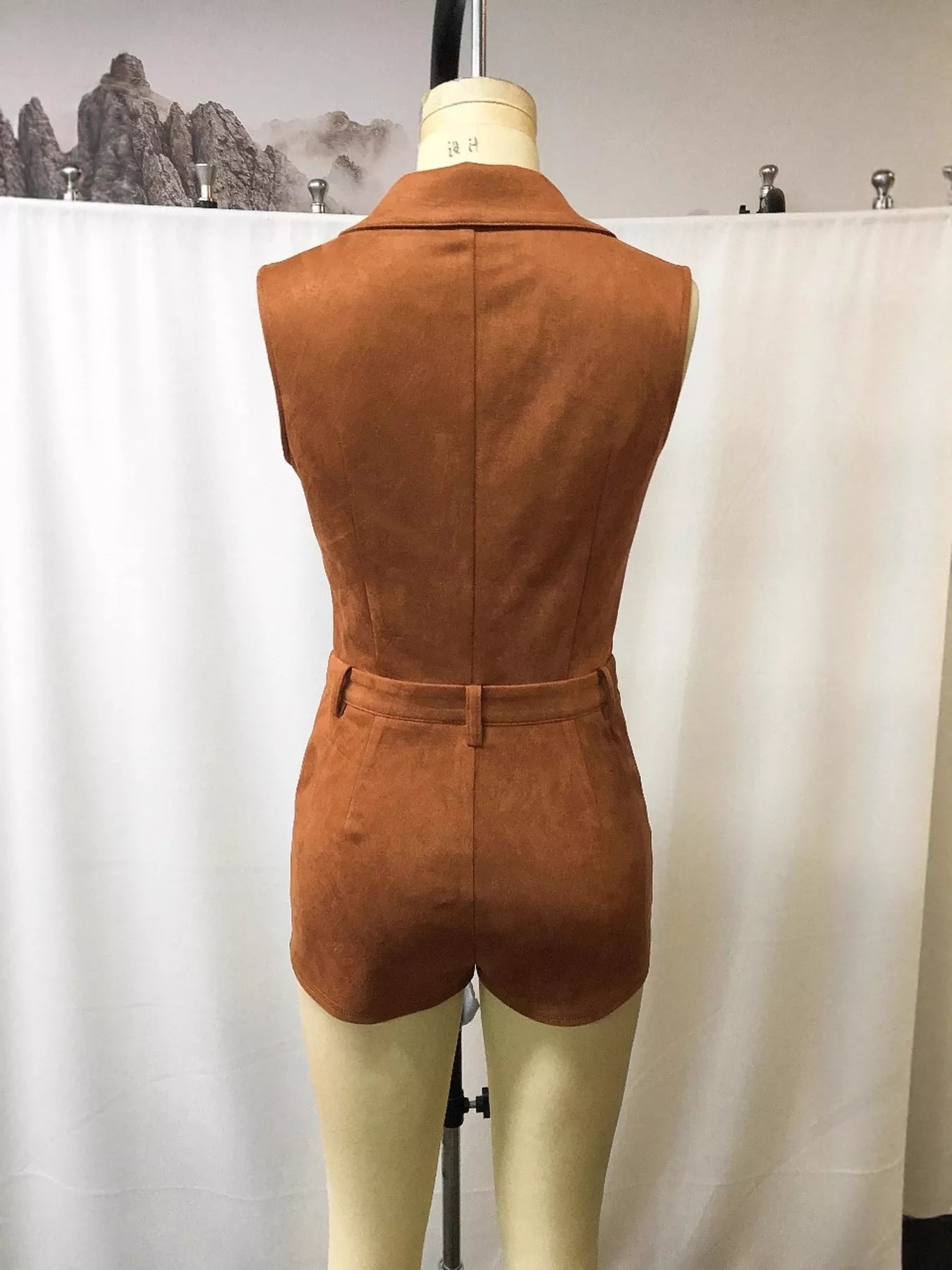 Brown suede romper on a mannequin against a white backdrop with mountain decorations.