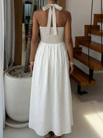 Woman wearing a white and beige dress with a halter neck design, standing indoors.