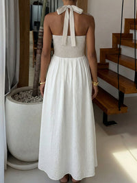 Woman wearing a white and beige dress with a halter neck design, standing indoors.