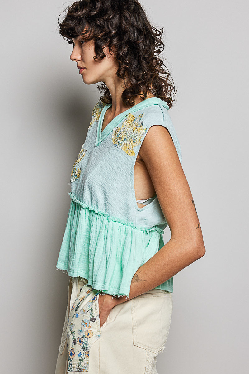 Woman wearing a light blue top with floral patterns on a plain background