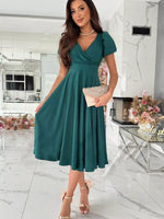 Woman in a teal dress holding a clutch in a modern interior setting