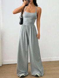 Woman wearing a gray jumpsuit against a white wall.