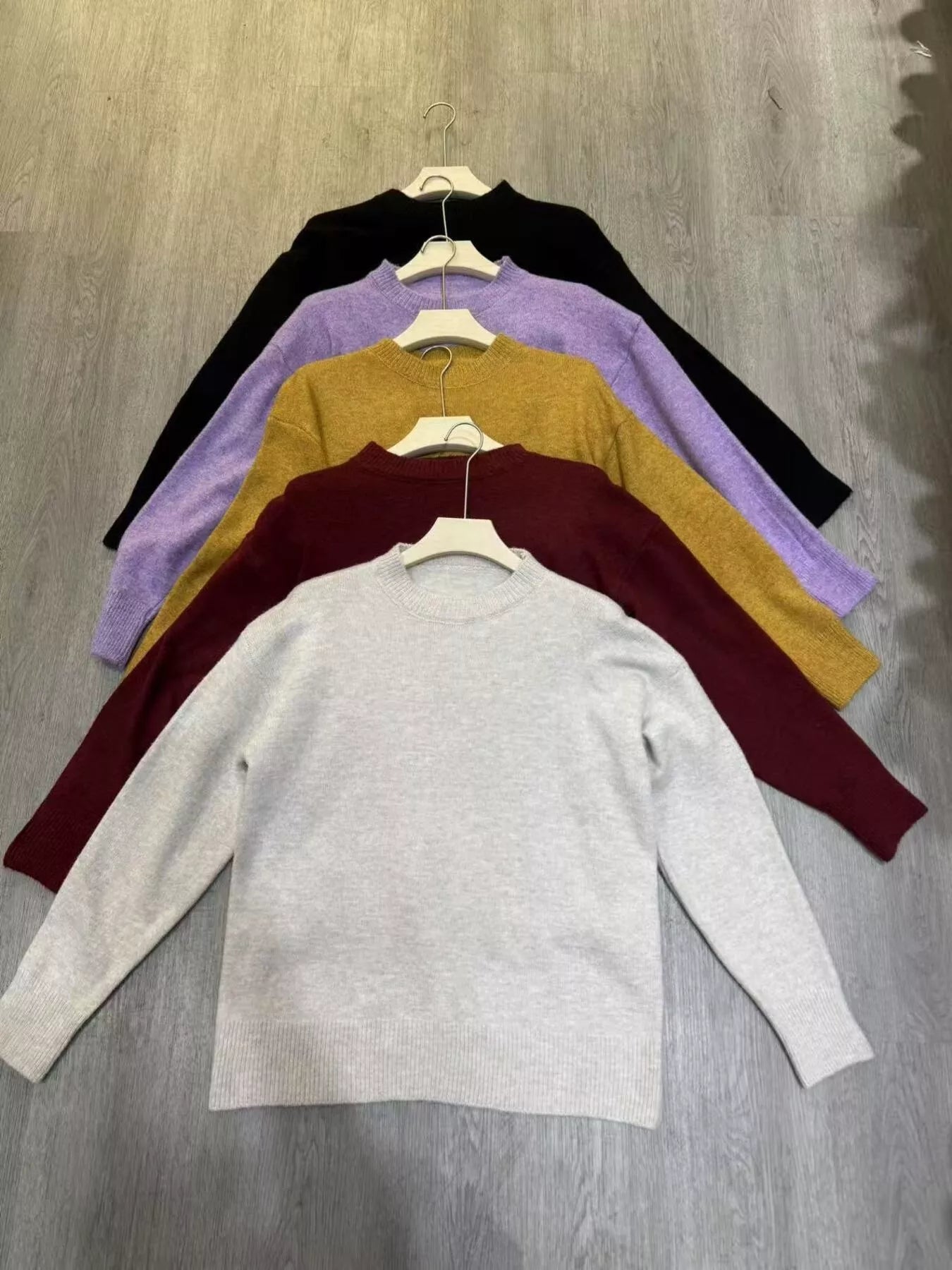 Stack of colorful sweaters on hangers against a wooden background