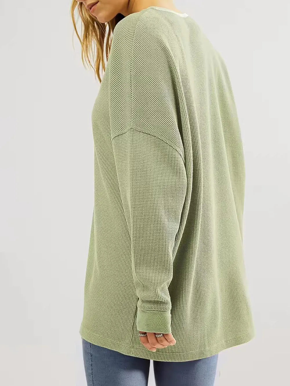 Green long-sleeve textured top worn by a person on a plain background