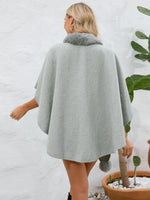 Woman wearing a gray cape with fur trim against a white wall.