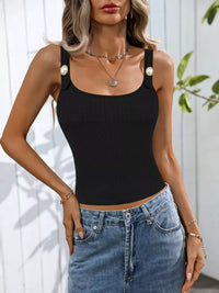 Woman wearing a black tank top with pearl straps and blue jeans against a white background