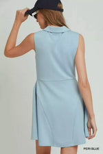 Woman wearing a light blue sleeveless dress with a navy cap on a plain background