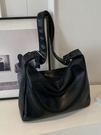 Black leather handbag on a light surface with a framed picture in the background