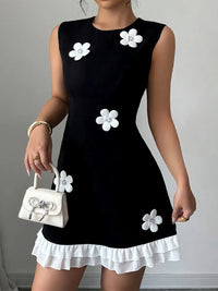 Black dress with white floral embellishments worn by a person, holding a matching white handbag.