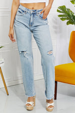 Person wearing light blue distressed jeans with a white background and yellow chair.